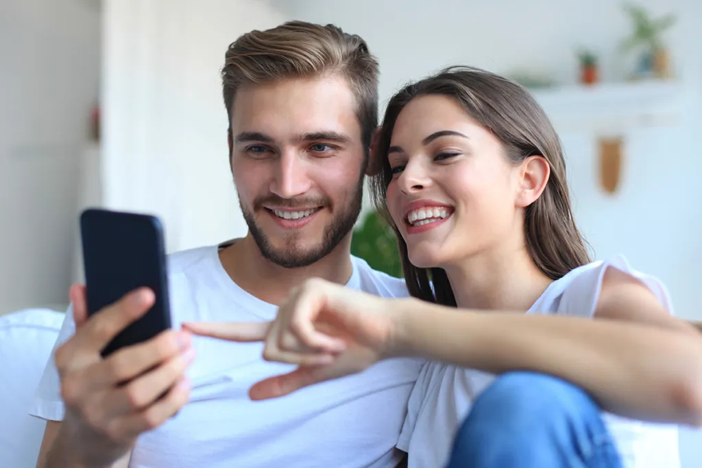 Man and woman smiling and pointing at phone